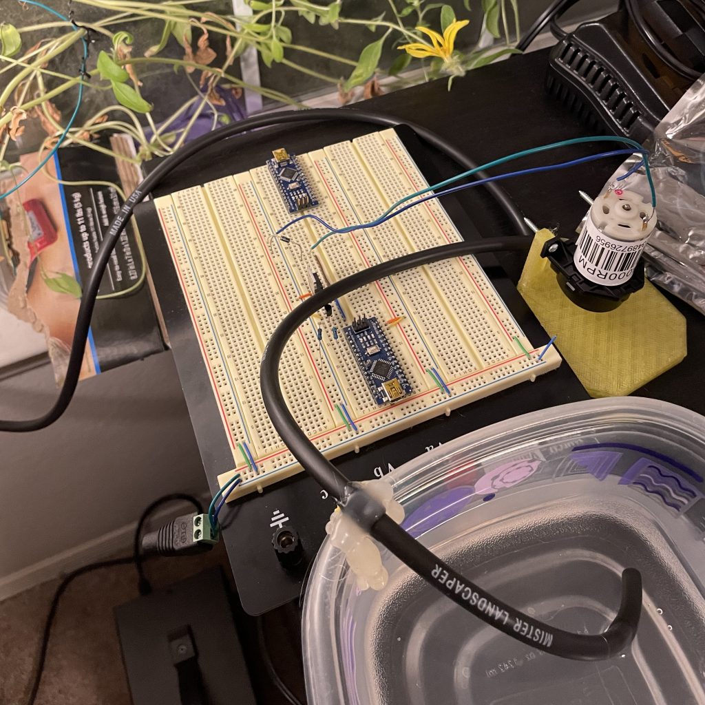 Bread board with some plants in the background. There is also a motor on the table and a small reservoir.